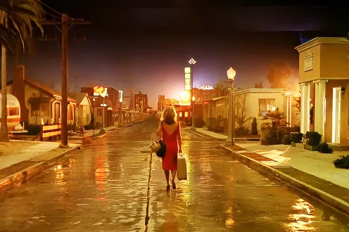 A woman stands in the middle of an empty city street in a red dress.