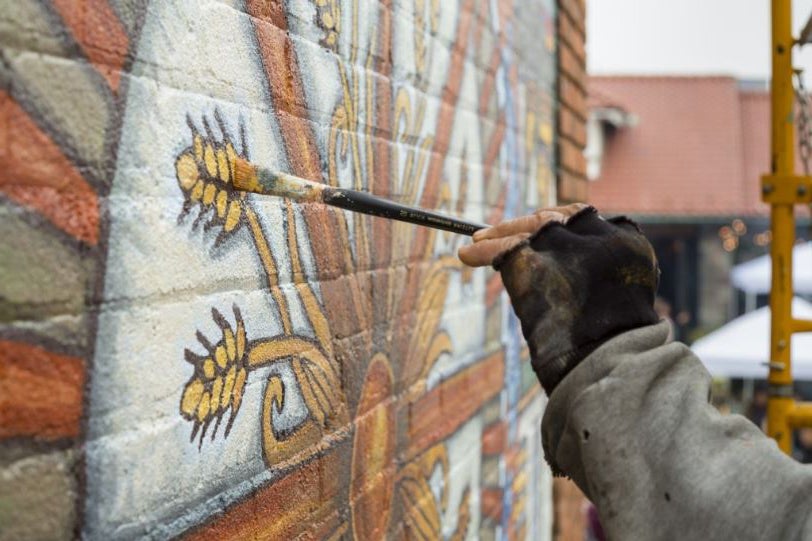A DIA Partners in Public Art partner artist paints stalks of wheat onto a mural