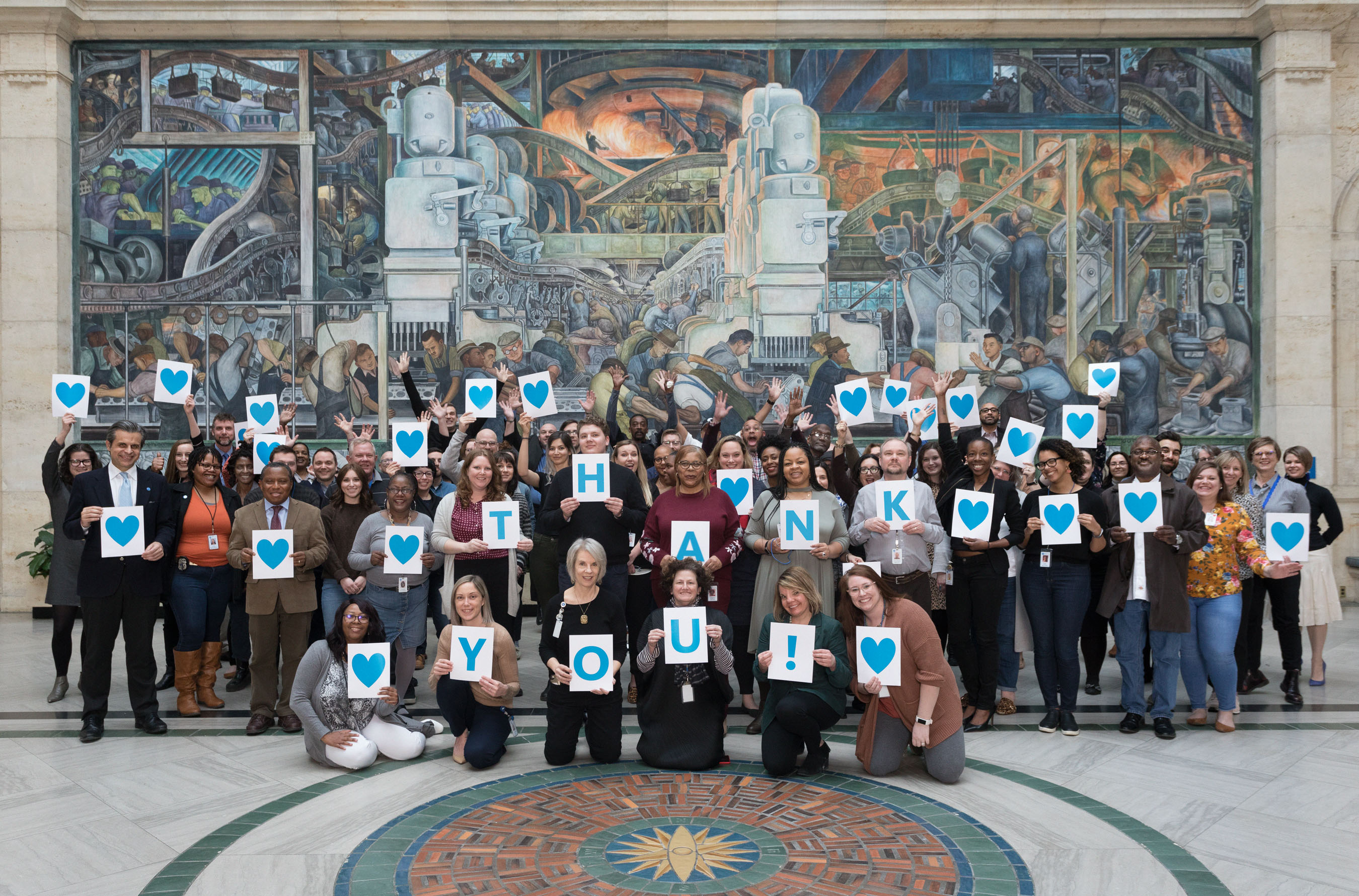 The staff of the DIA pictured in Rivera Court holding signs that say "Thank You"