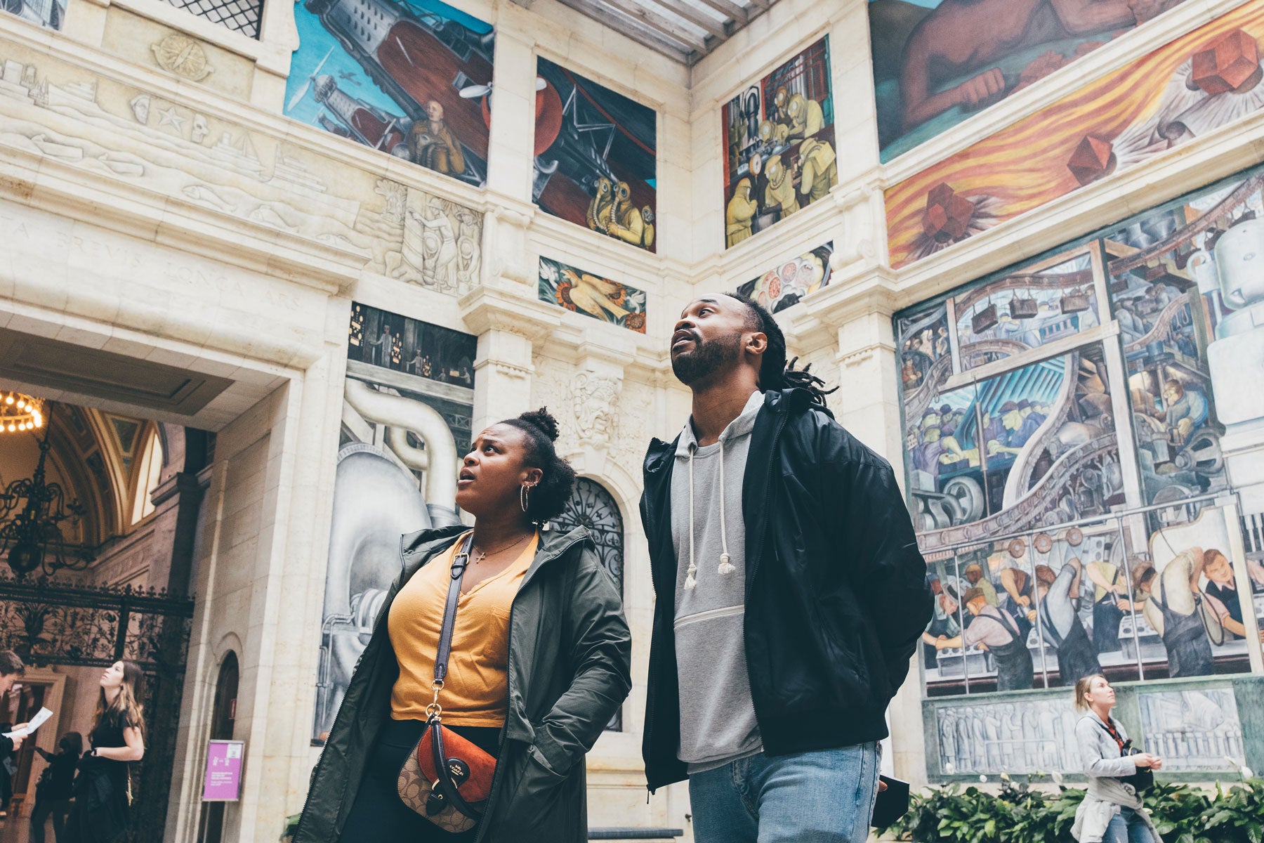 A man and a woman staring in awe at Diego Rivera's Detroit Industry Murals