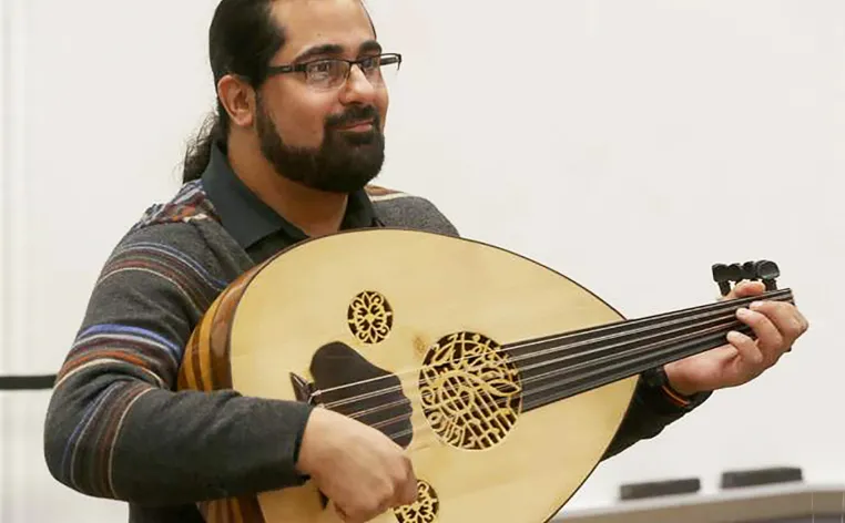 A man with his hair in a ponytail and beard plays a lute.