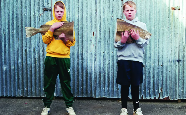 Two young boys holding one half of a large fish