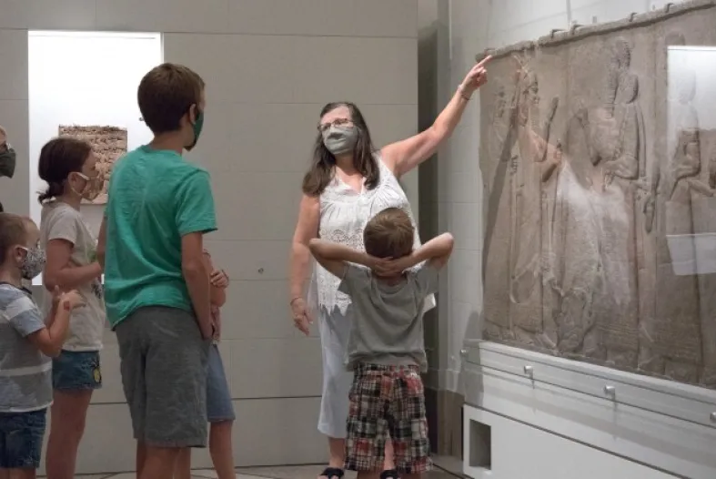 A lady pointing at a framed art while children look at her.