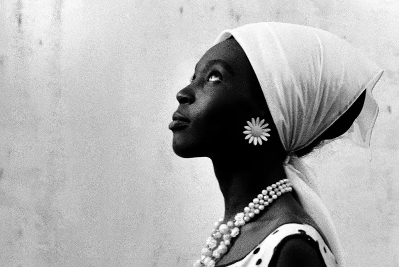 A black woman wearing a large flower earring and a scarf on her head looks up and to the left.