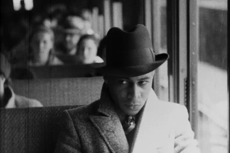 A man sitting on a bus in a coat, suit and hat