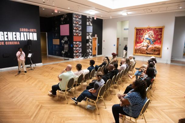 Audience watching a poetry reading in front of a gallery