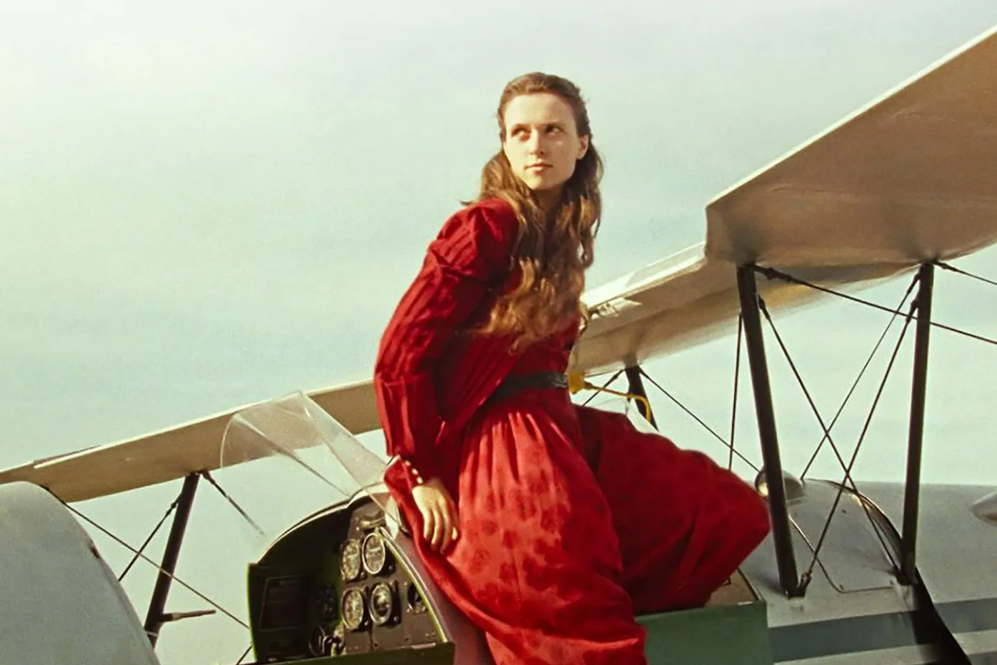 A woman in a red dress sits on a small plane