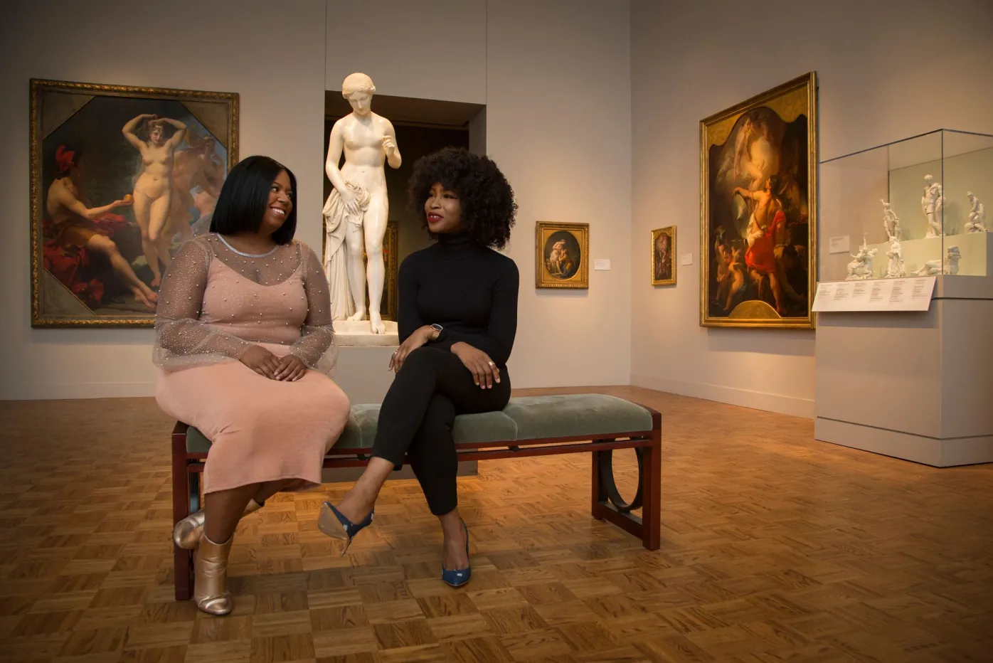 Two women sit on a bench in a gallery in the Detroit Institute of Arts