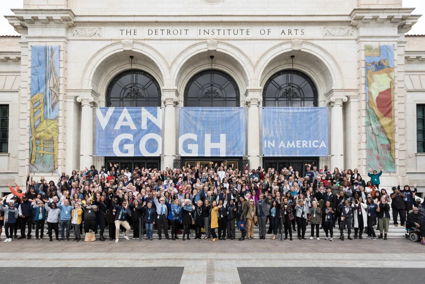 Detroit Institute of Arts staff pose together on the front steps of the museum under a banner that reads &quot;Van Gogh in America.&quot;