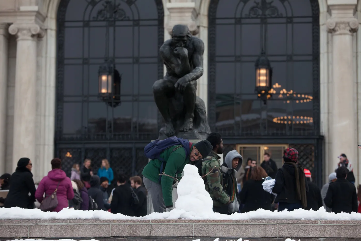 The Thinker in the snow and a man in front, fixing up a small snowman