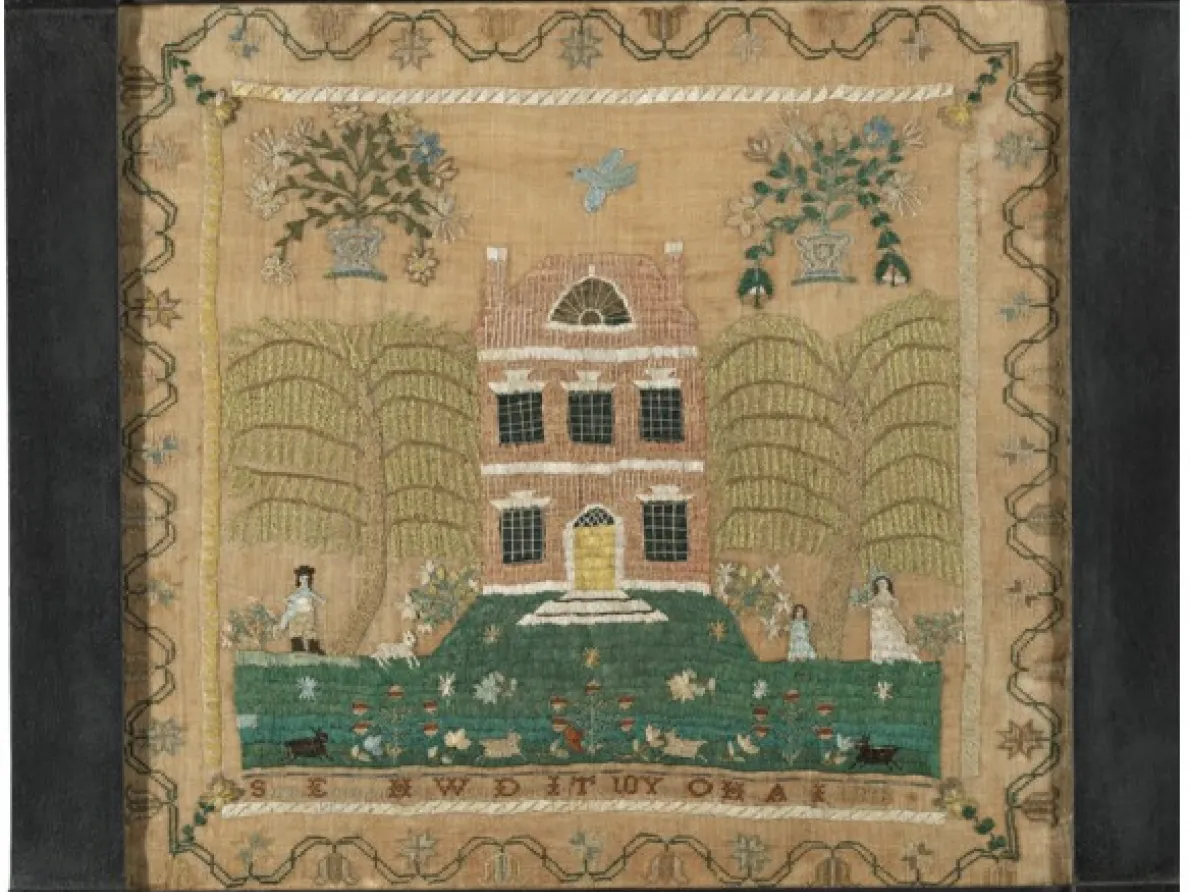 Needlework of a pink building on a green landscape in a black frame. 