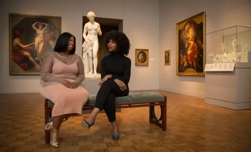 Two women sit on a bench in a gallery in the Detroit Institute of Arts