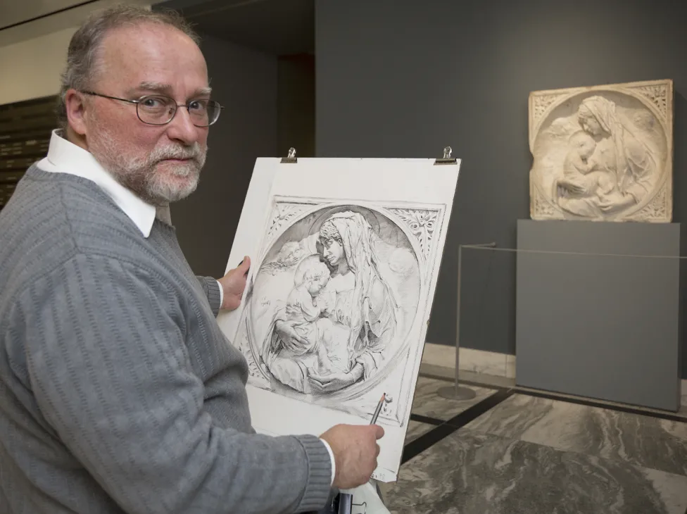 An older man in a sweater and collared shirt holds up his drawn recreation of a sculpture