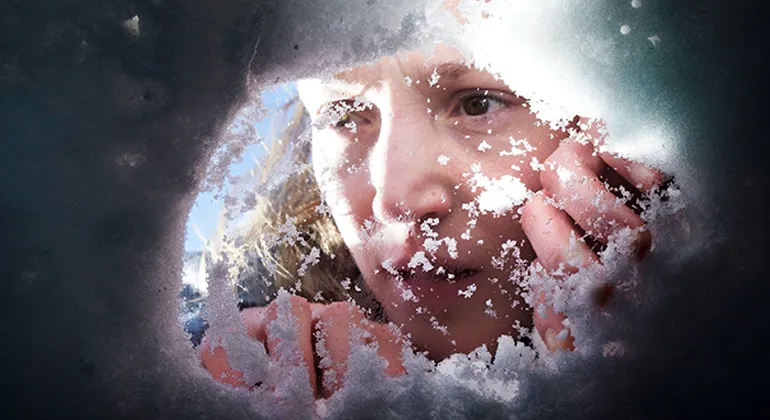 A woman peering through an opening made in the snow with her hands