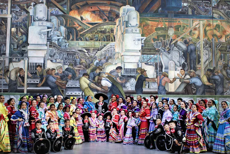 Members of Ballet Folklorico de Detroit posing together in front of the DIA&#039;s Detroit Industry Murals