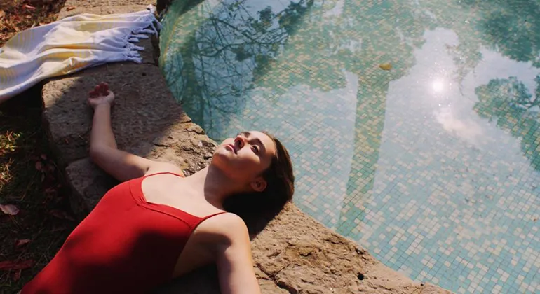 A woman in a red bathing suit suns herself on the edge of a small tiled pool