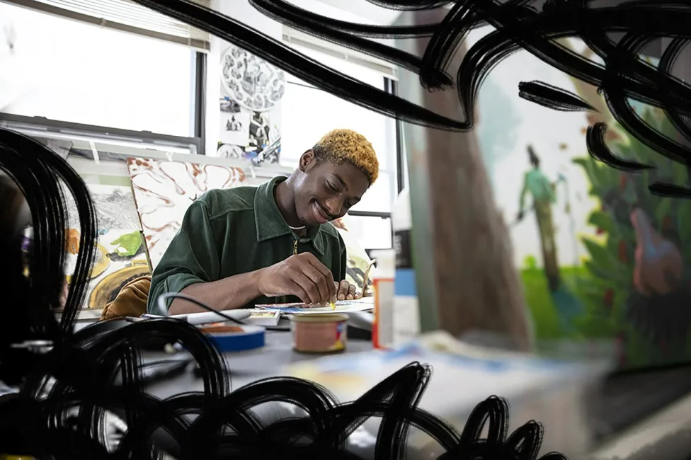 Habacuc S. Bessiake making art in a room surrounded by his works