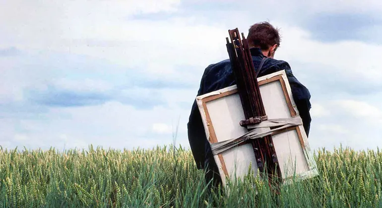 A man standing in a field while holding an easel and canvas on his back