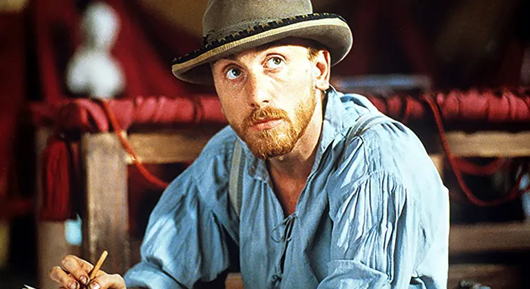 An actor portraying Van Gogh in a loose blue collared shirt and hat.