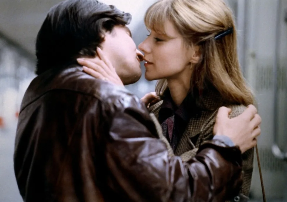 A man and a woman embrace each other before kissing while wearing brown leather jackets