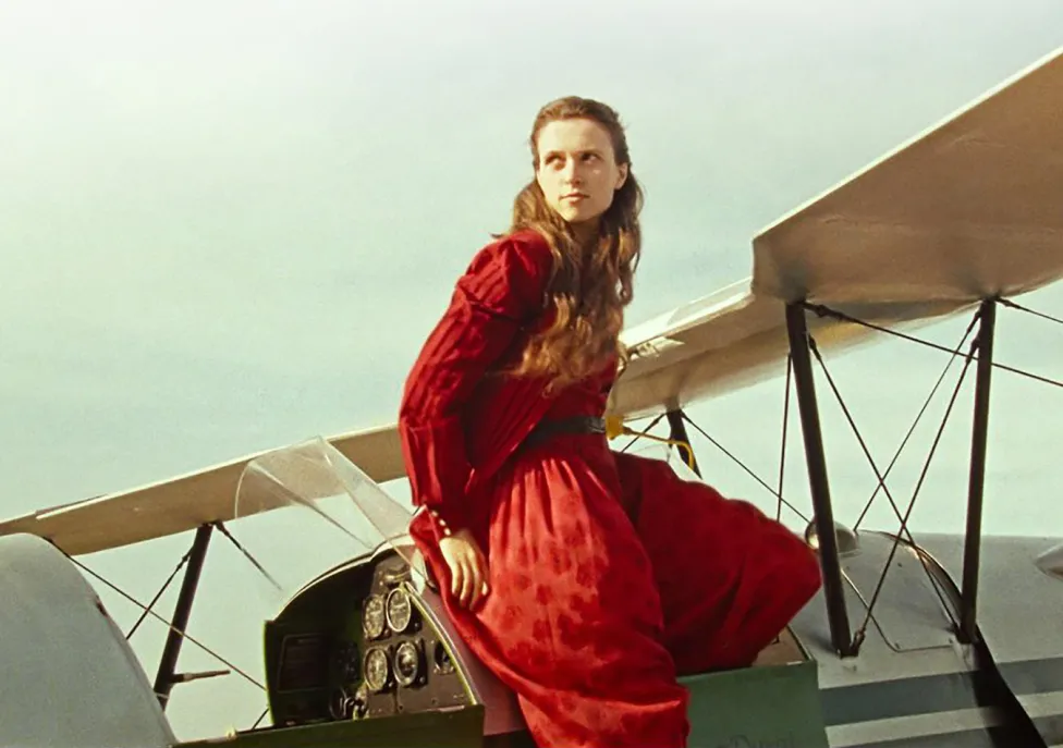 A woman in a red dress sits on a small plane