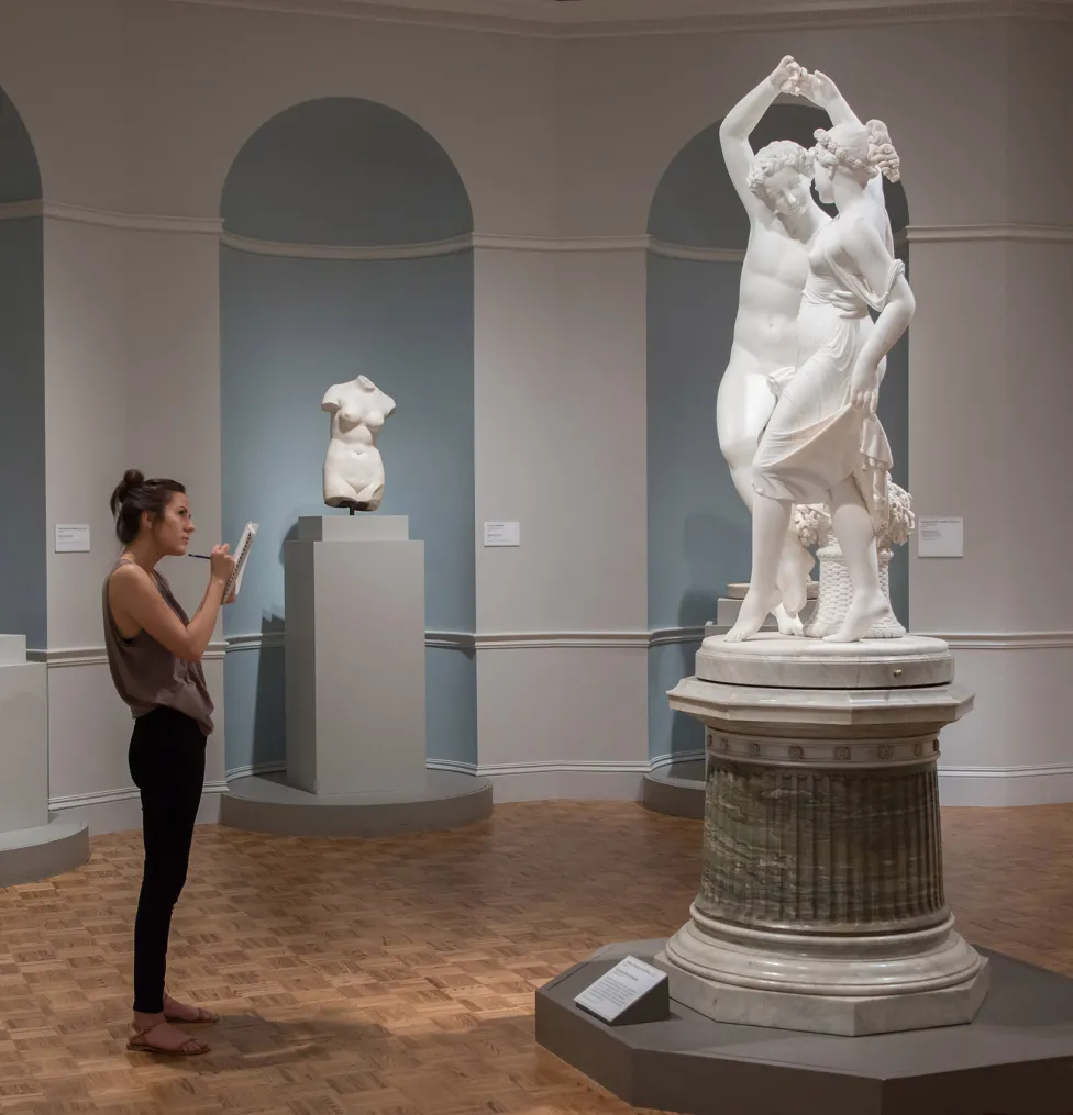 A woman stands with a sketchbook while looking at a statue in the Italian Art galleries.
