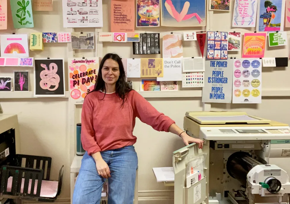 Rachel Delmotte poses in jeans and a red sweatshirt in their studio.