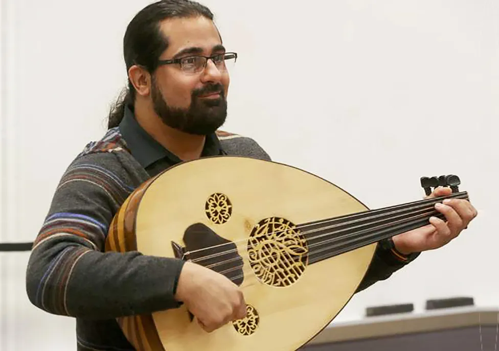 A man with his hair in a ponytail and beard plays a lute.