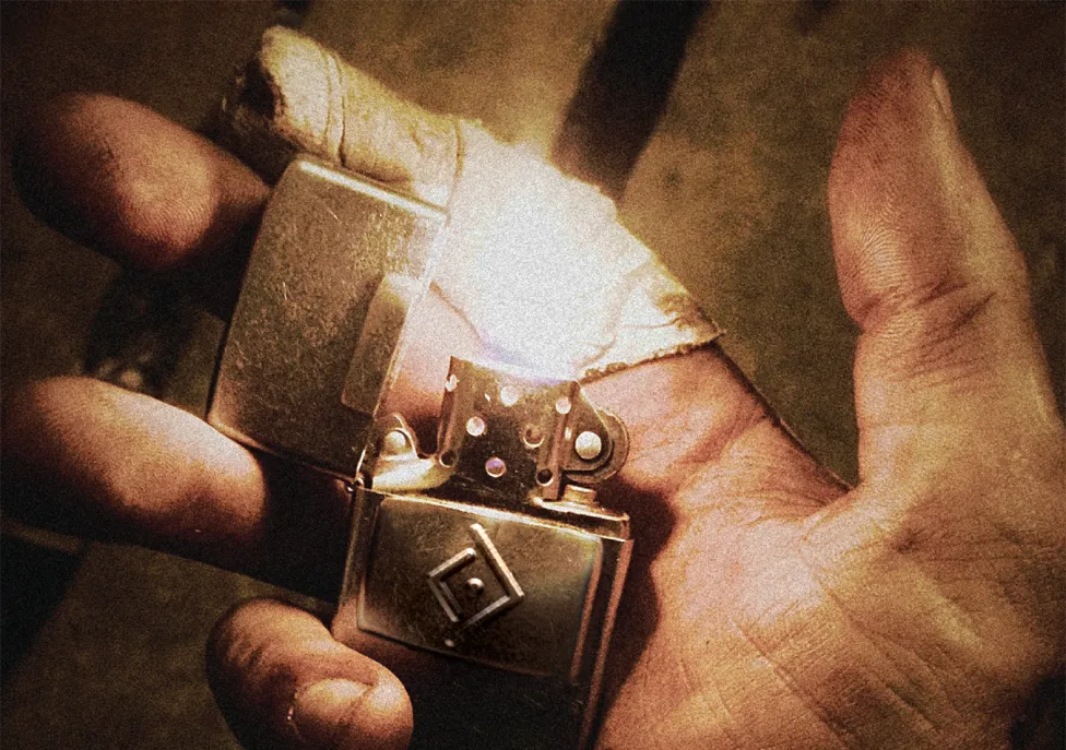 A metal lighter being lit in the palm of an open, dusty hand.