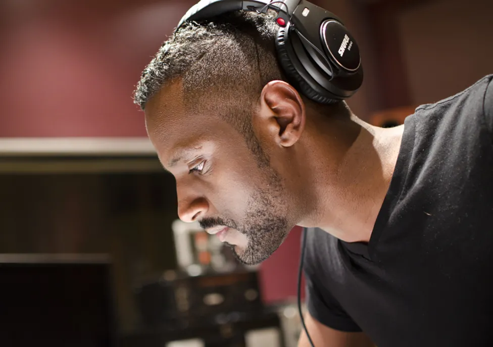 Carlos Simon pictured in a recording studio wearing large over-the-ear headphones.