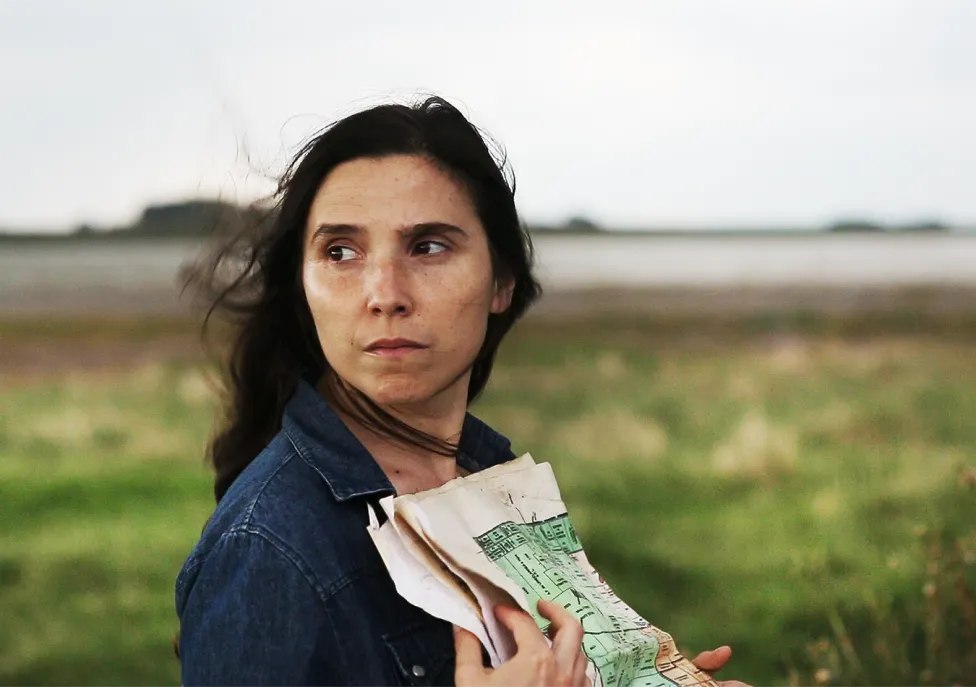 A woman looks around forlornly and clutches a paper map to her chest.