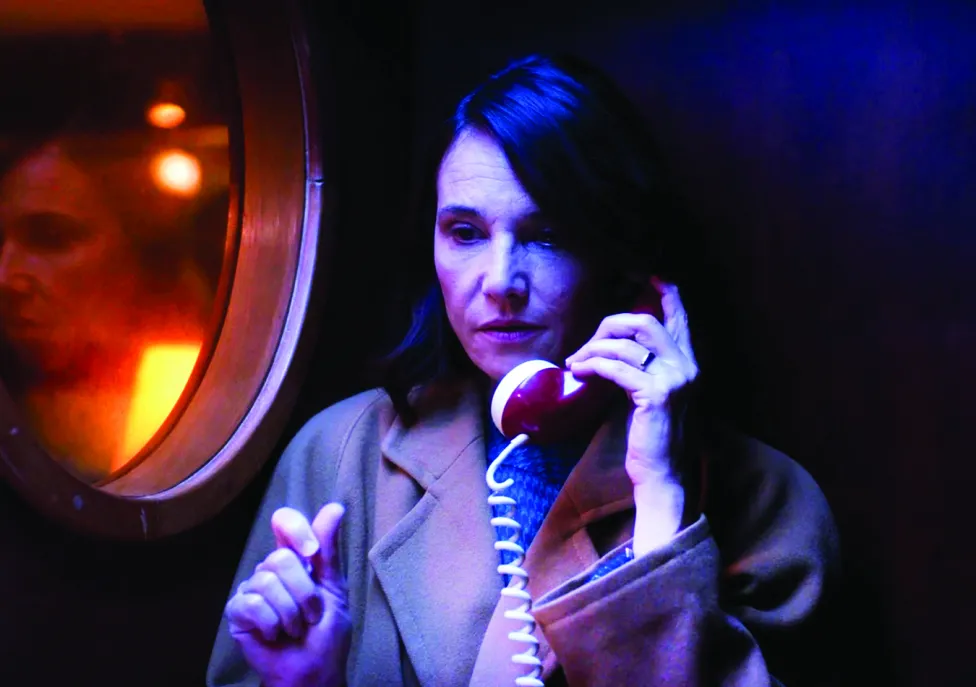 A woman in a brown coat talks on an older-style, corded phone.