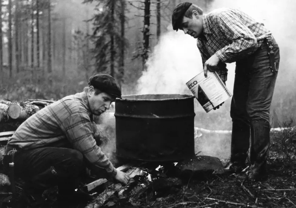 Two men working over a barrel used as a fire pit.