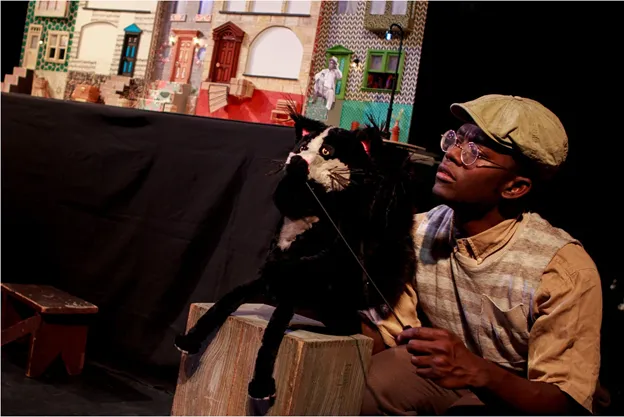 A boy operates a black and white cat puppet