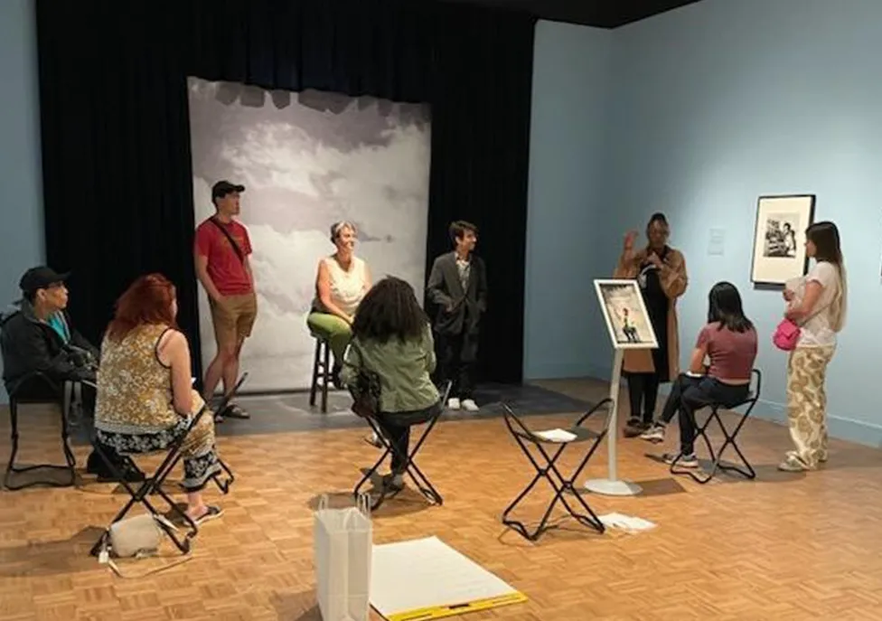 Members of Inside Out Literary Arts and workshop attendees sit around the photo studio in the exhibition James Barnor: Accra/London--A Retrospective.