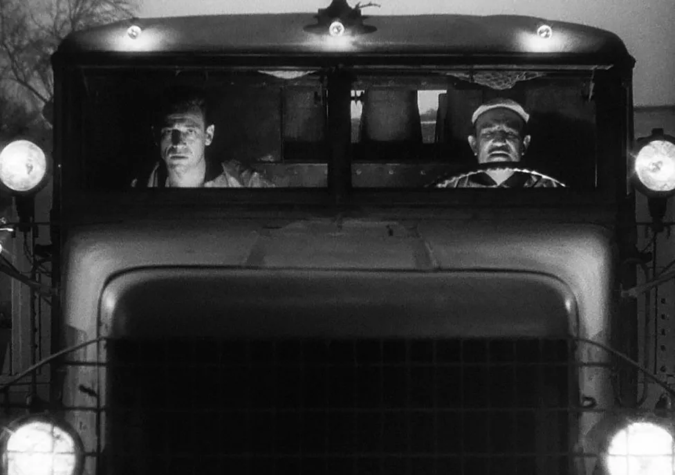 The front end of a truck with men sitting in the passenger and drivers seats.