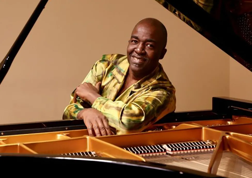 A man sits, smiling at an open piano.