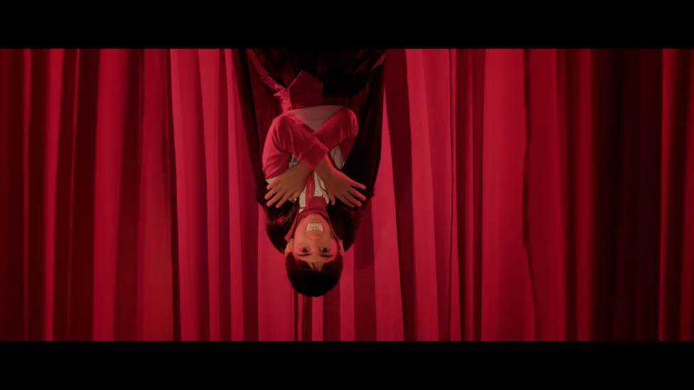 A child dressed as dracula hangs upside down in front of a drawn red stage curtain.