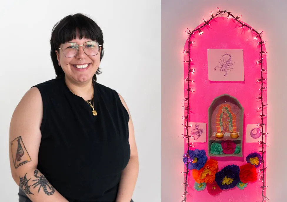 A person in a black tank top with black tattoos next to a lighted, pink altar they created.
