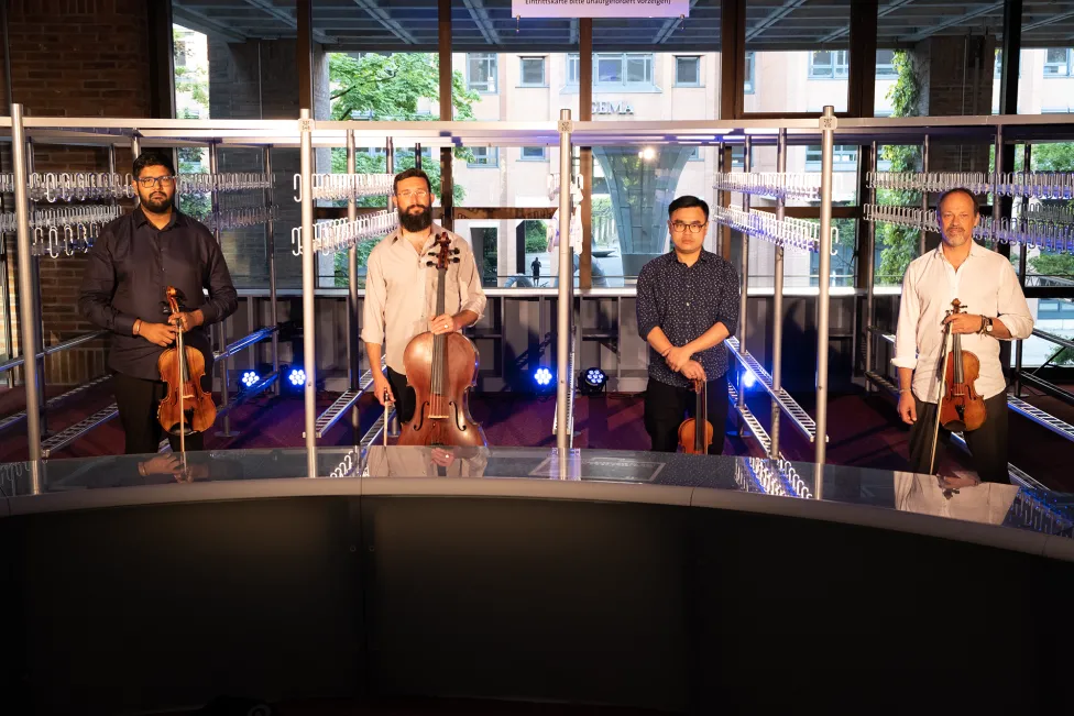 Four band members pose with their instruments in individual glass sections.