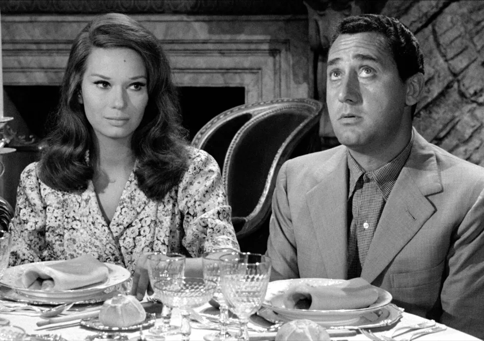 A black and white image of a man and a woman sitting at a round dining table during a meal.