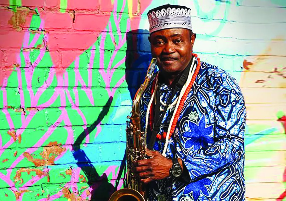 A man in a colorful shirt and hat holds onto a saxaphone