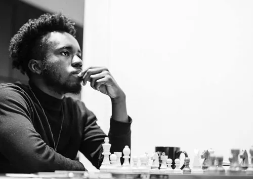 A young man sits at a table playing chess