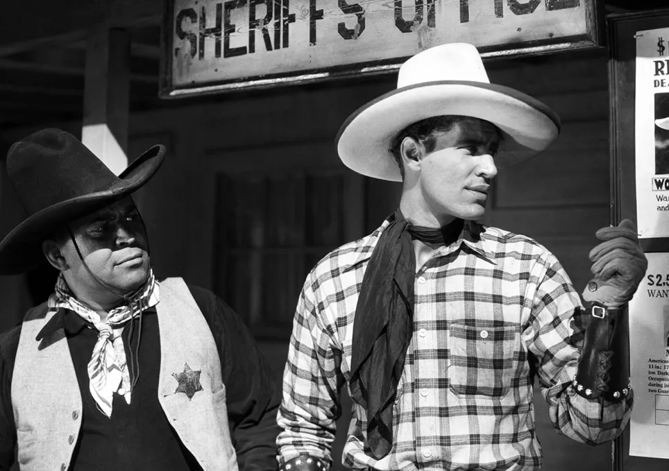 Two men in cowboy and sheriff costuems for a black and white film.