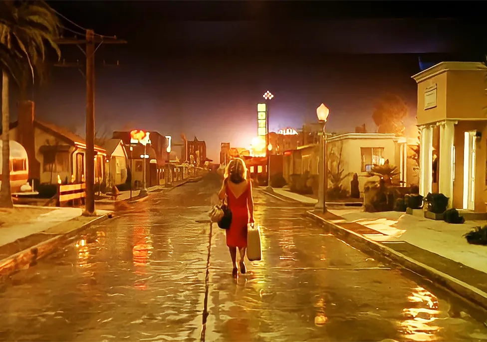 A woman stands in the middle of an empty city street in a red dress.