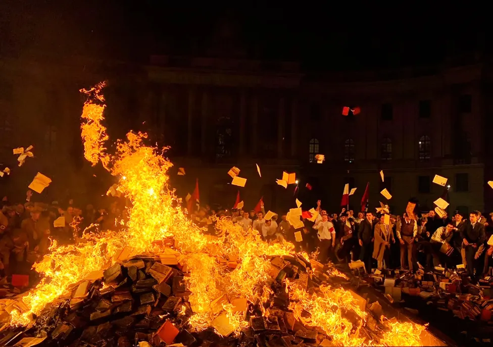 People gathered around a large fire throwing in books