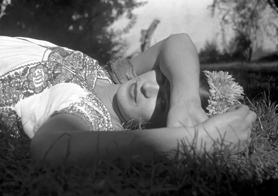 Frida Kahlo laying on grass with her arm covering her eyes from the sun.
