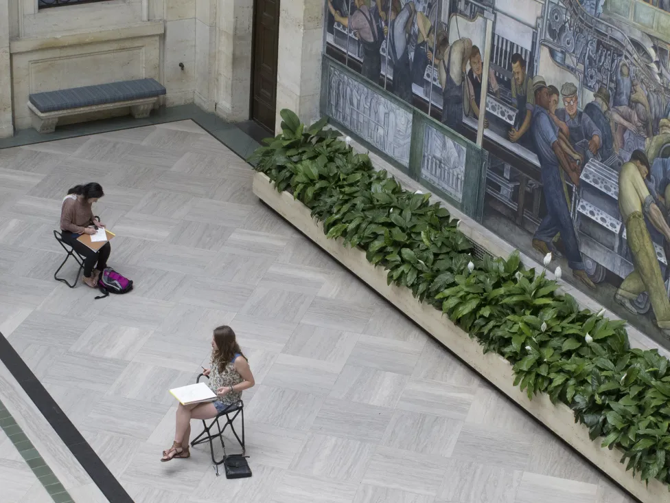 Patrons drawing while sitting on gallery stools in the DIA's Rivera Court