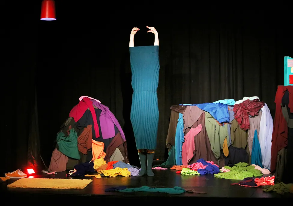 A stage full of colorful clothes and someone getting stuck getting dressed.