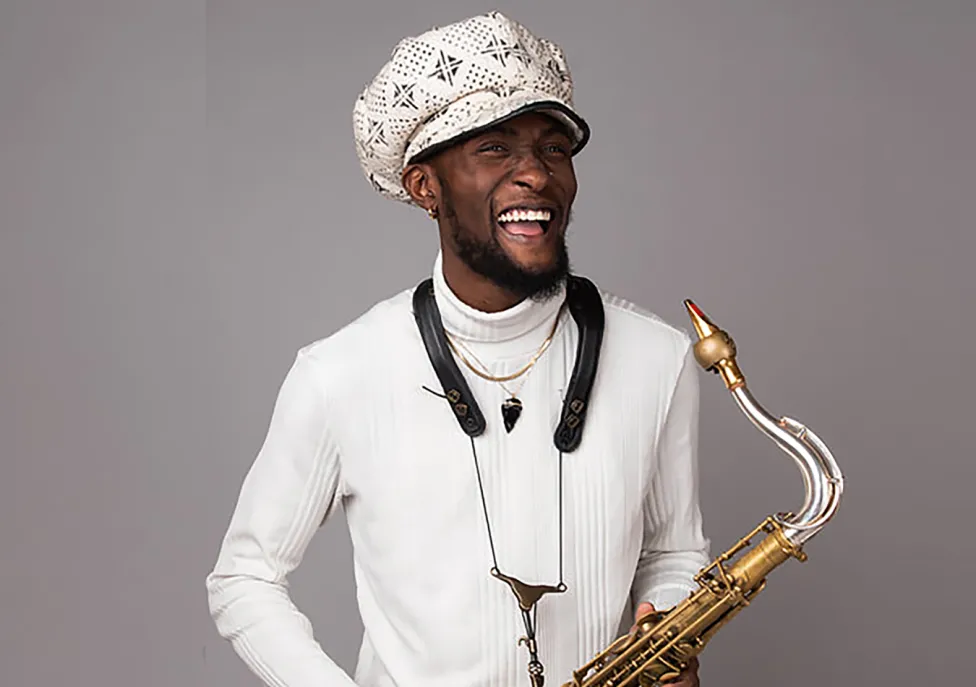 Isaiah Collier poses in a white hat and shirt with a saxophone